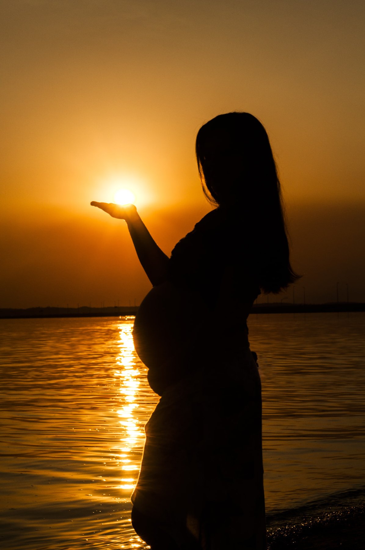 Expectant mother at sunset holding the setting sun in her palm before a prenatal sound therapy session